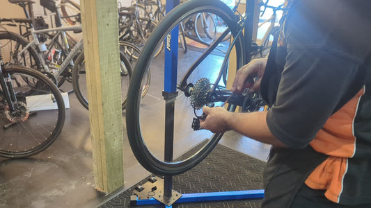 Bike Clinique mechanic working on a road bike rear wheel and cassette in a truing stand at the workshop