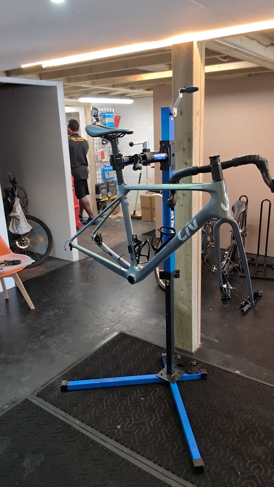 A teal Liv road bike frame without wheels held in a blue repair stand inside the Bike Clinique workshop