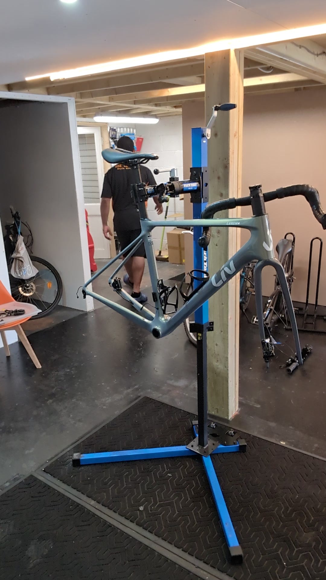 Drop-bar bike frame and fork held on a blue workstand in the Bike Clinique workshop, with wheels removed